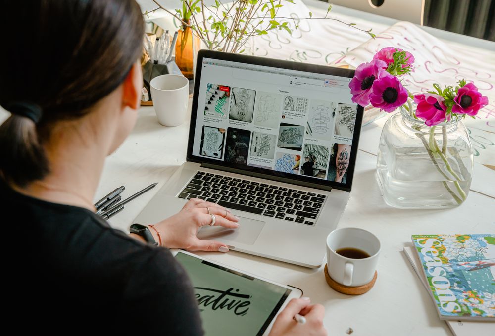 A creator researching ideas at a laptop on a bright desk.